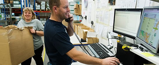 Mies puhuu puhelimeen ja käyttää tietokoneita varastoon. Nainen liikkuva laatikko.